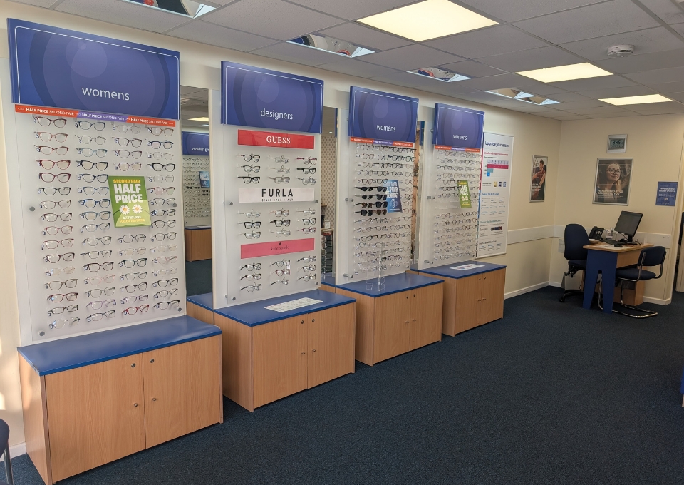 Eyewear display panels labeled women's and designer brands with rows of glasses in a bright optical shop.