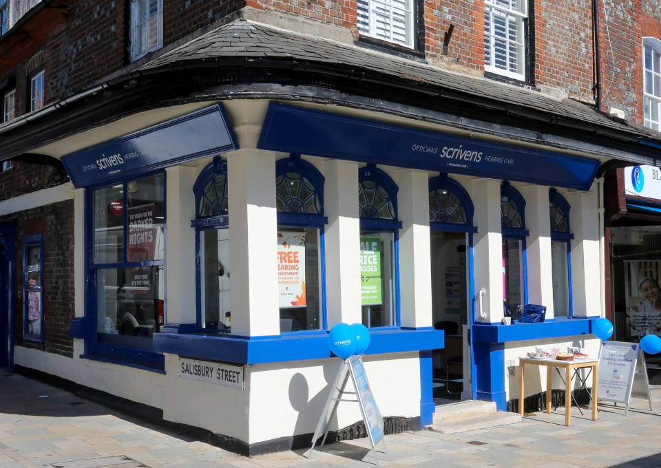 Blue-and-white optician shop on Salisbury Street with blue awnings, balloons, and a display table outside.