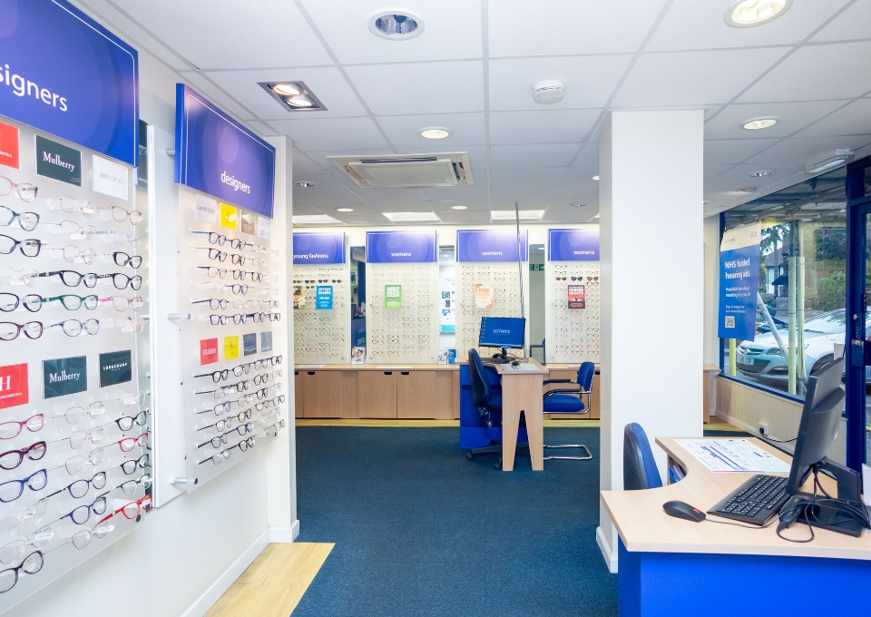 Bright optical store interior with wall-mounted glasses displays and a front desk in the foreground.