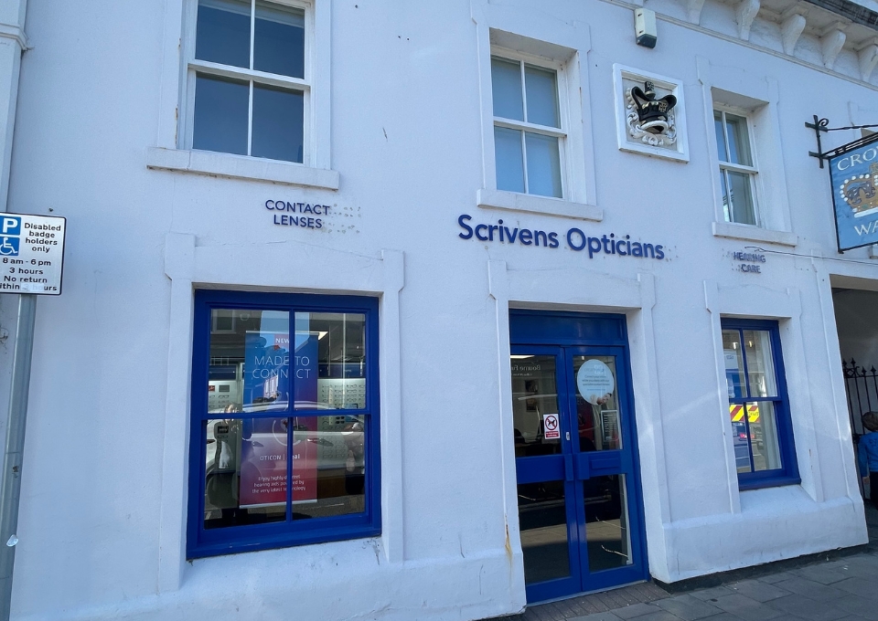 Exterior of a light-blue storefront for Scrivens Opticians with blue doors and windows; sign reads 'Scrivens Opticians' above the entrance.