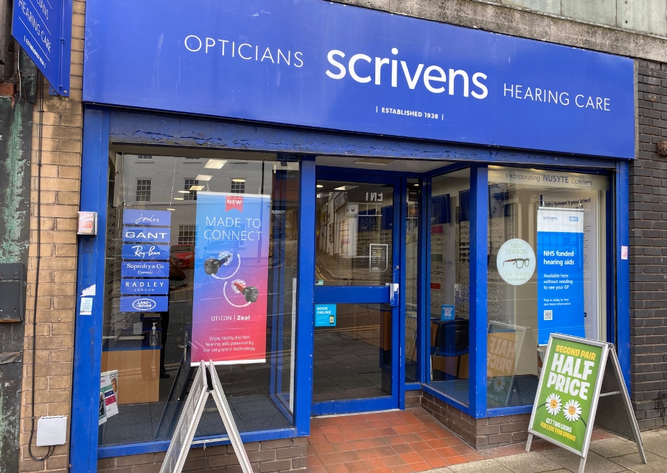 Blue storefront for Scrivens Hearing Care opticians, with 'Opticians' and 'Hearing Care' signage above the entrance and blue-framed glass doors.