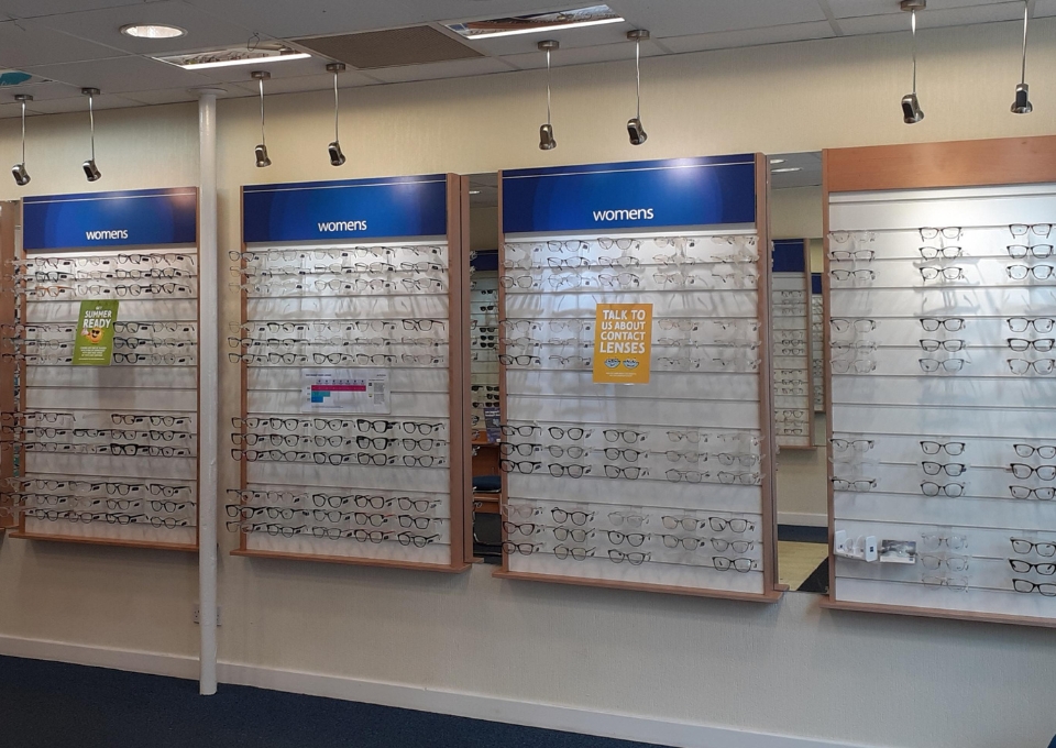 Wall of women's eyeglasses on wooden display panels in a store section.