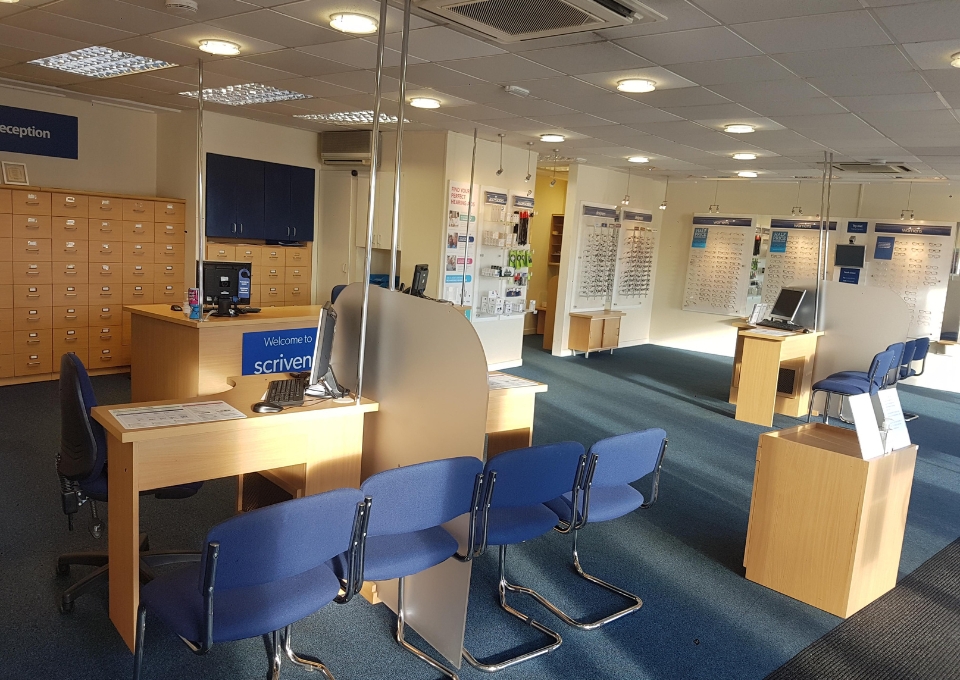 Reception area with a curved wooden front desk, a computer, and a row of blue chairs facing the desk.