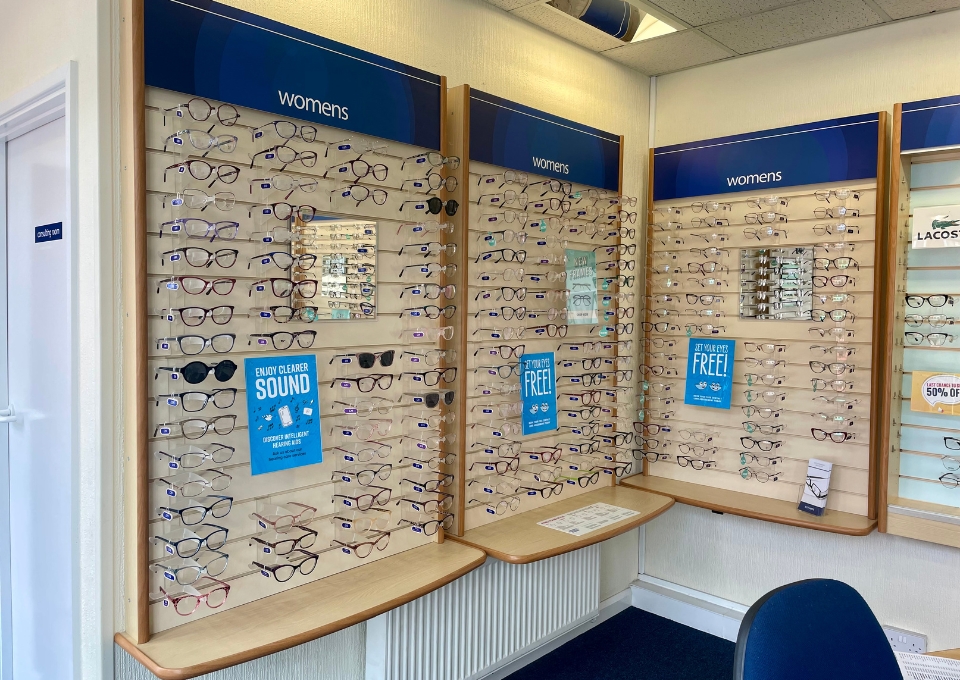 Wall of women's eyeglasses on display panels with blue 'womens' signs above.