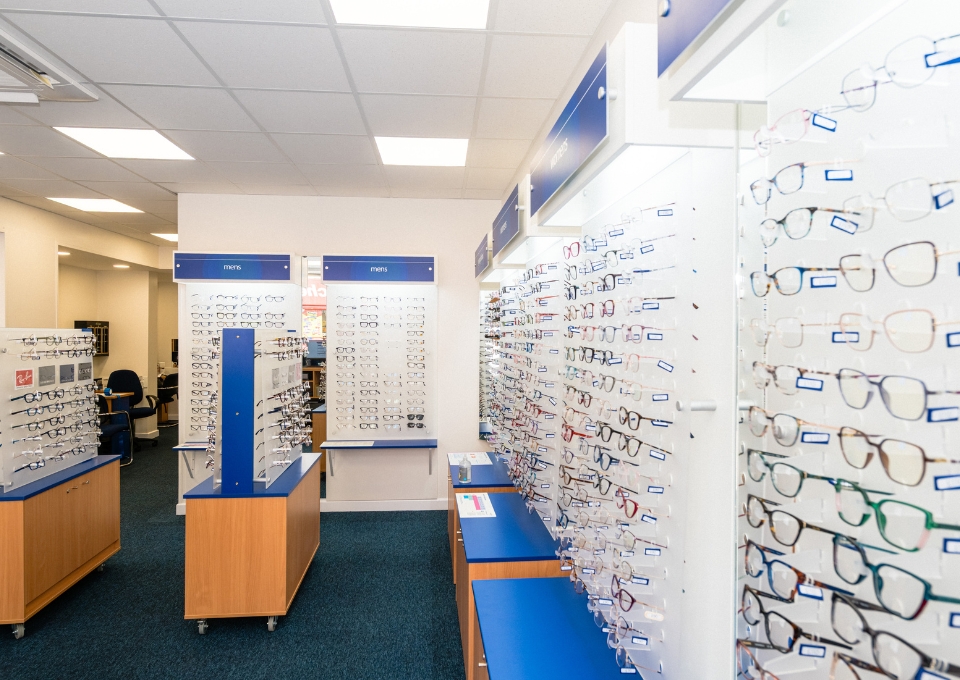 Bright optical shop with walls of eyeglasses on racks and blue display units in a well-lit space.