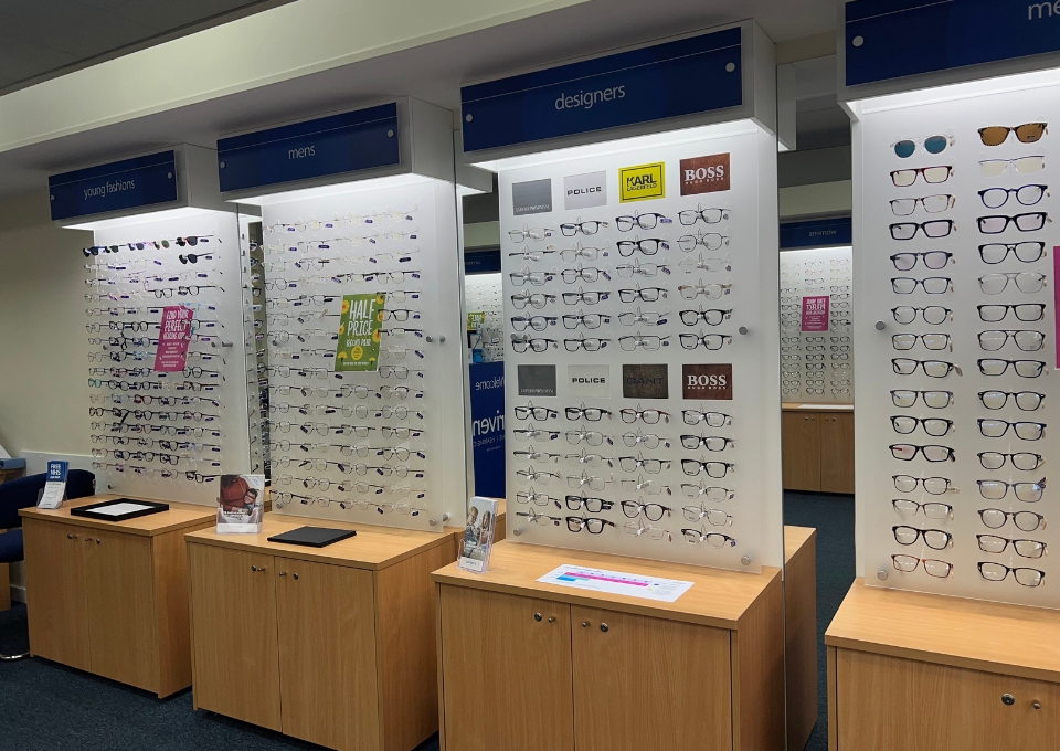 Eyewear store display: rows of glasses on white panels with blue category signs for 'young fashions', 'mens', and 'designers'.