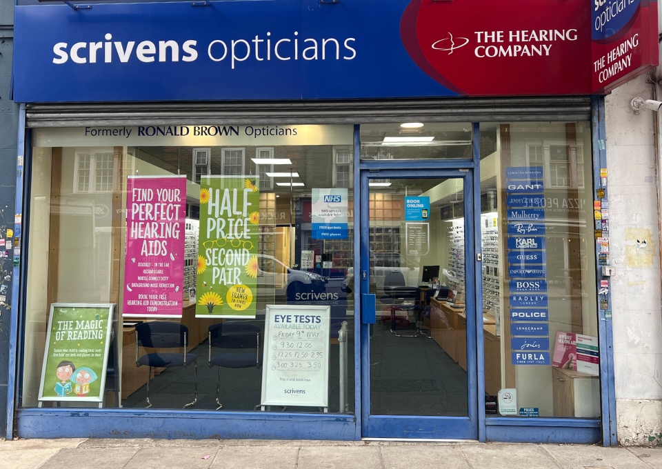 Exterior view of a Scrivens Opticians storefront with blue signage and a red Hearing Company logo above the door.