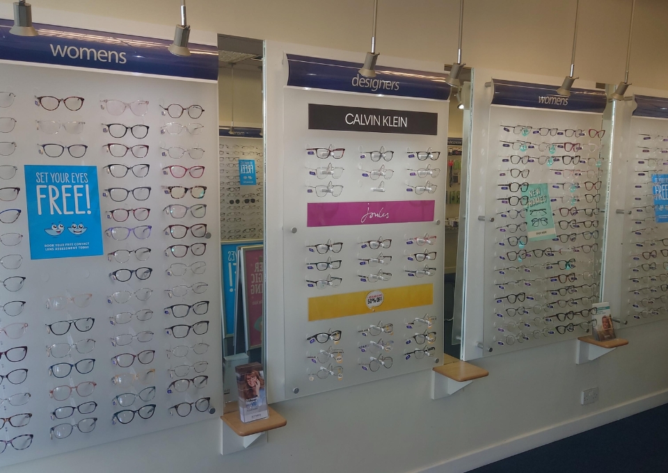 Wall of women's designer eyeglasses on display panels, including Calvin Klein frames.