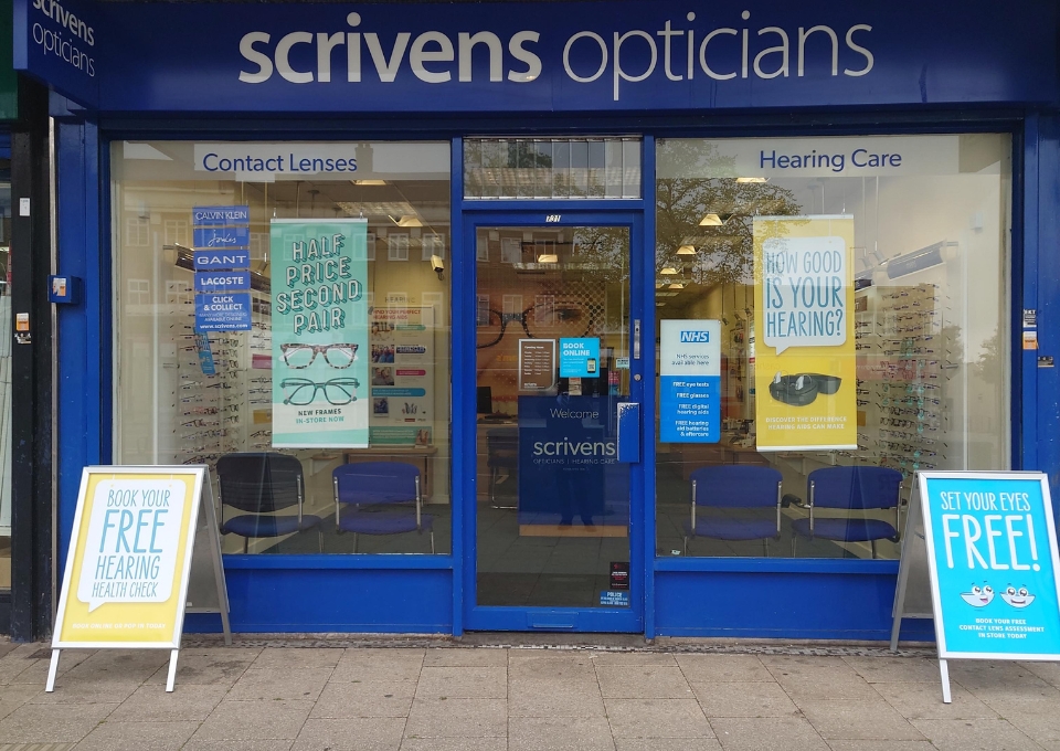 Blue Scrivens Opticians storefront with 'Contact Lenses' and 'Hearing Care' signs in the windows.