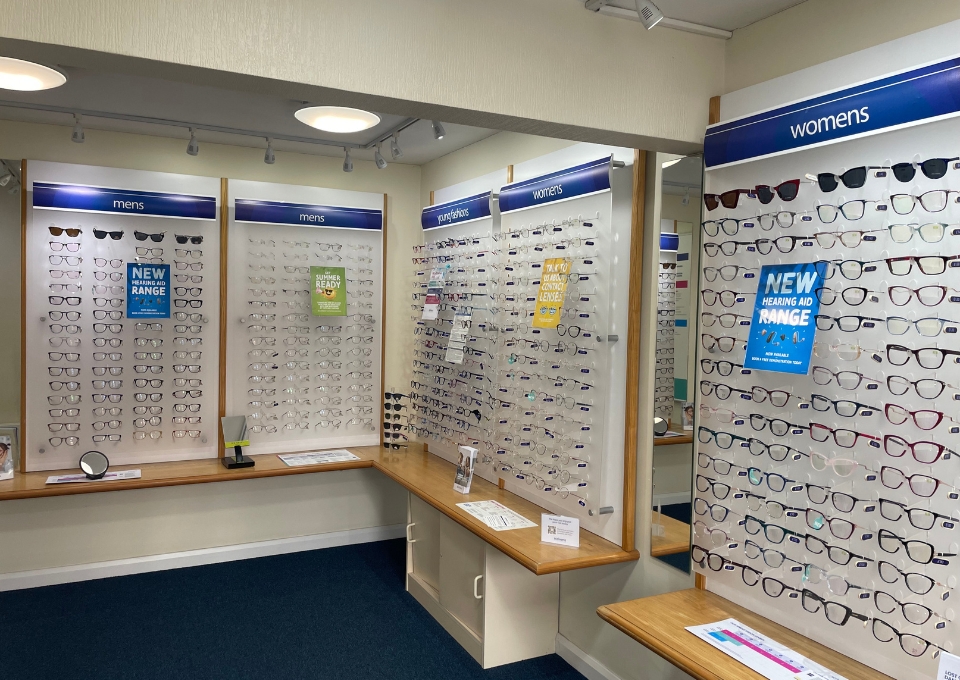 Indoor optical shop with wall displays of eyeglasses labeled 'mens' and 'womens'