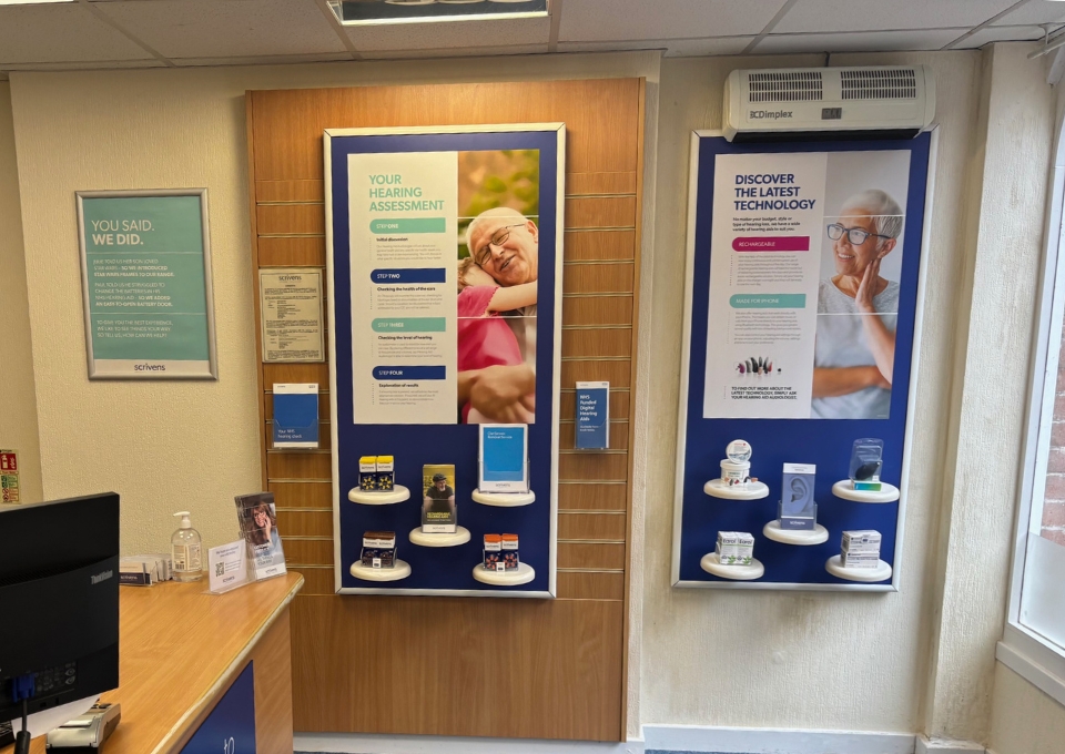 Interior of a clinic with blue display boards showing hearing care information and product samples on small shelves on a wooden panel wall.