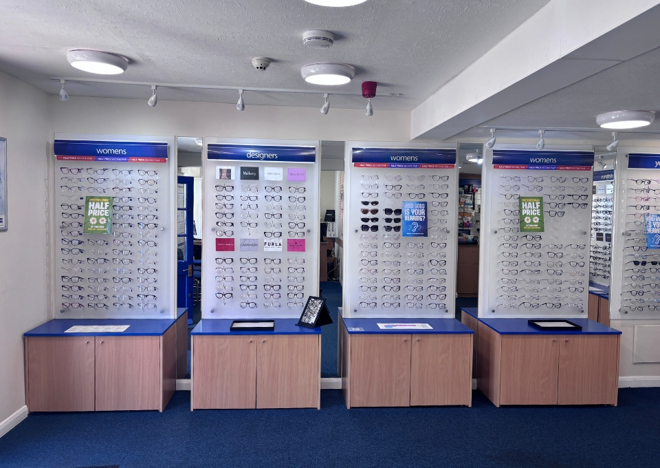 Eyewear showroom with four display panels of glasses on wooden cabinets, labeled women and designers, in a storefront store.
