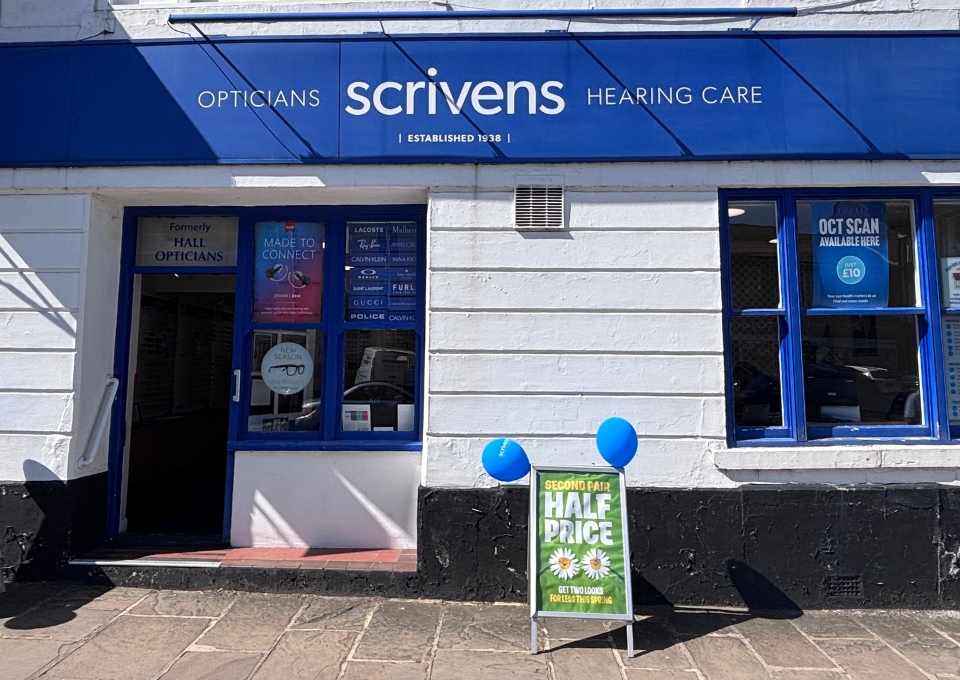 Blue and white Scrivens Opticians storefront with open door, posters in the left window, and a half-price sign with blue balloons outside.