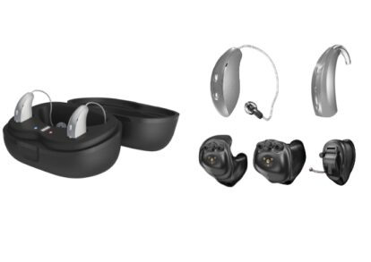 Open charging case with two wireless earbuds inside; several hearing-aid components and domes laid out nearby (ear molds, BTE parts).