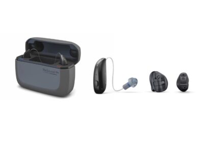 Hearing aids with an open charging case and three ear pieces laid out in a row, from left to right: case, behind‑the‑ear model, and two ear tips.