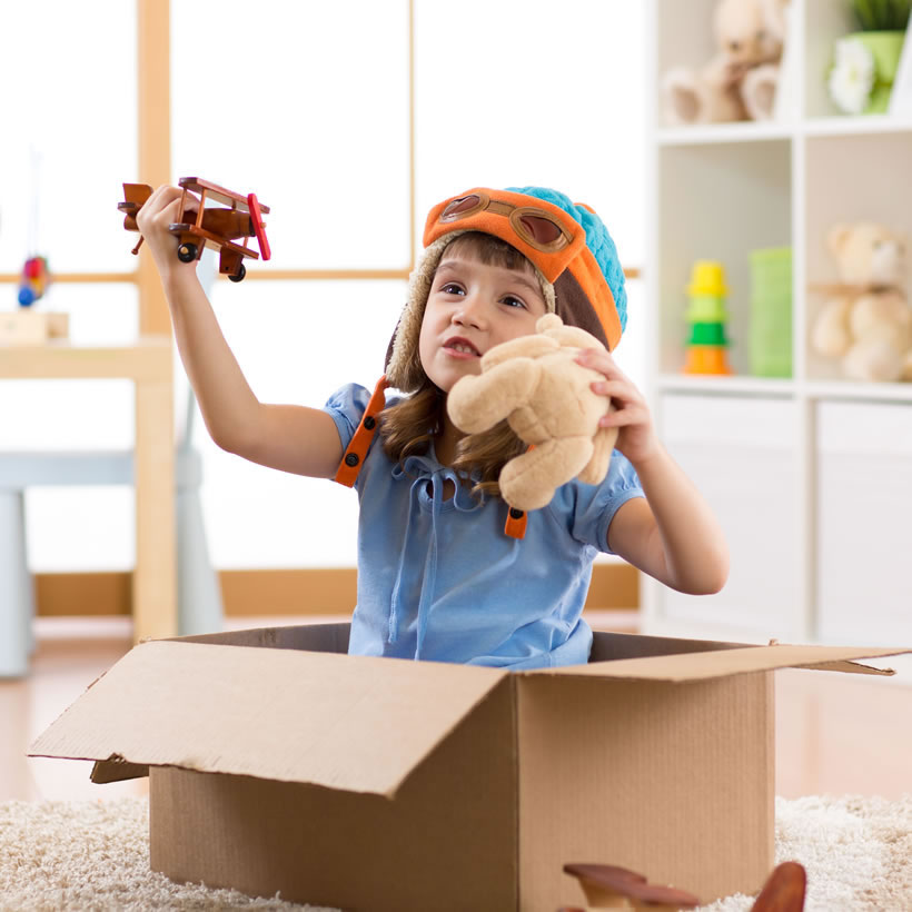Kid playing in a box with a airplane and a teddy bear