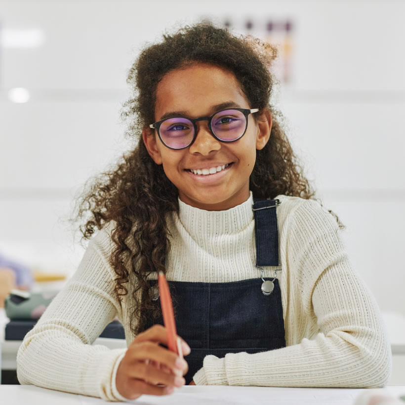Happy girl in dungarees sat at a table drawing