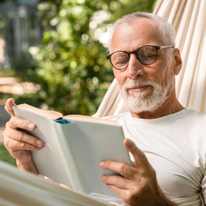 Older man in glasses reading a book while relaxing in a hammock