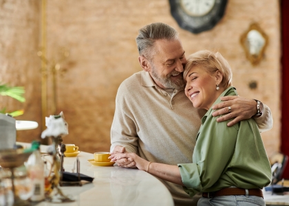 Man and woman embracing wile stood at a coffee shop table