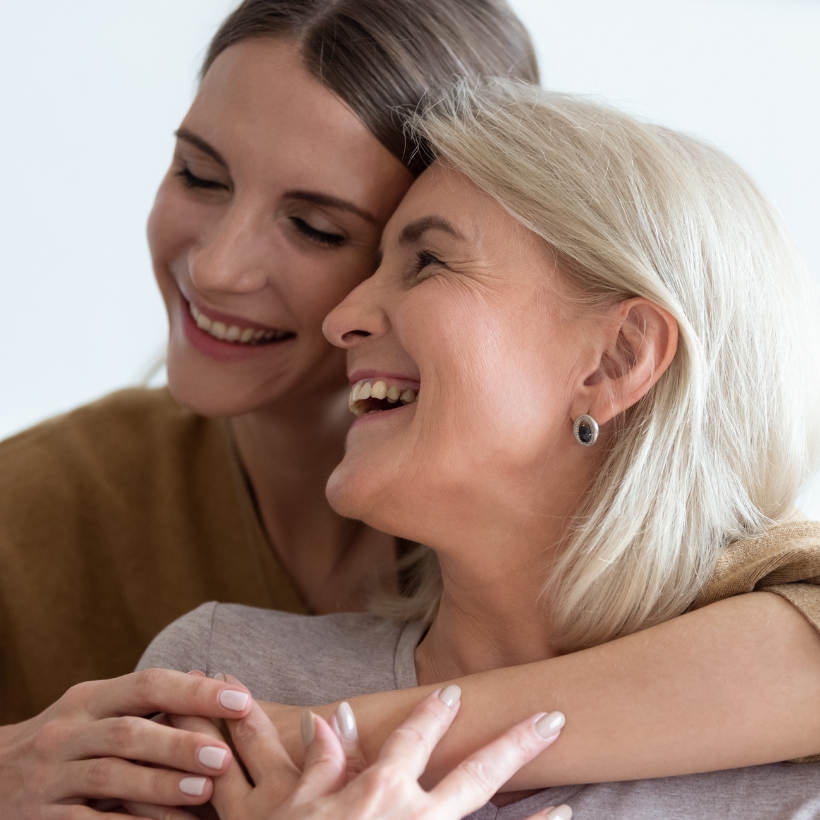 Elderly woman and middle aged woman embracing and holding hands