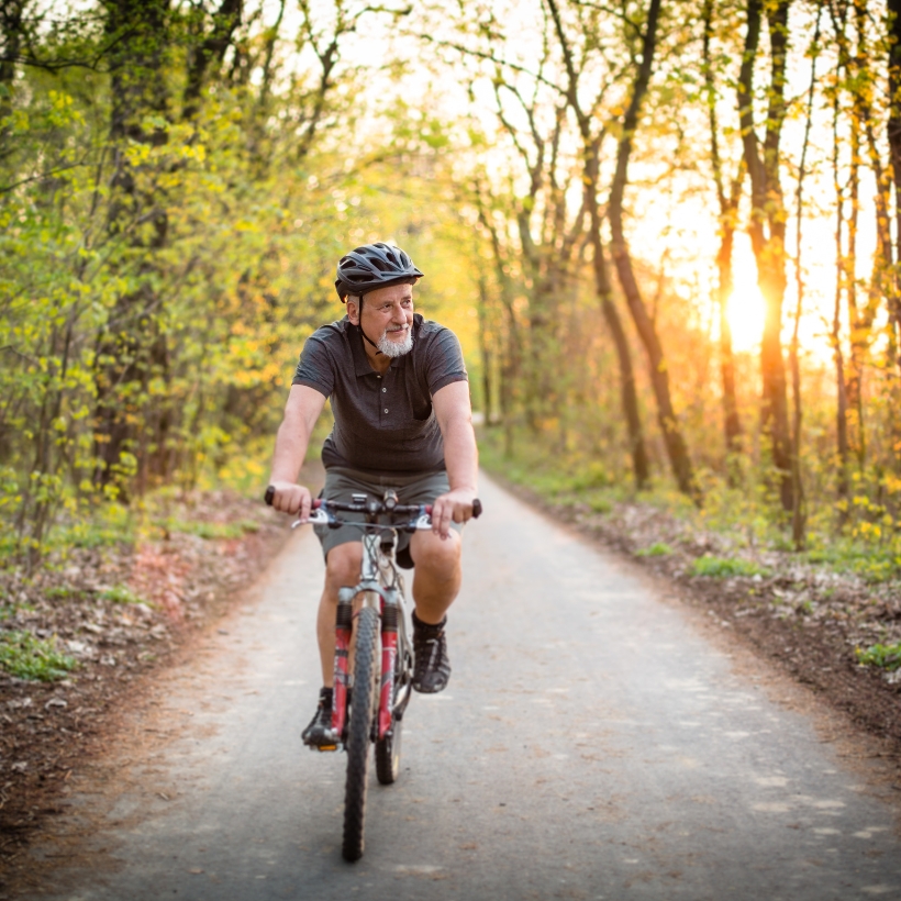 Older man riding a bike on a forest path