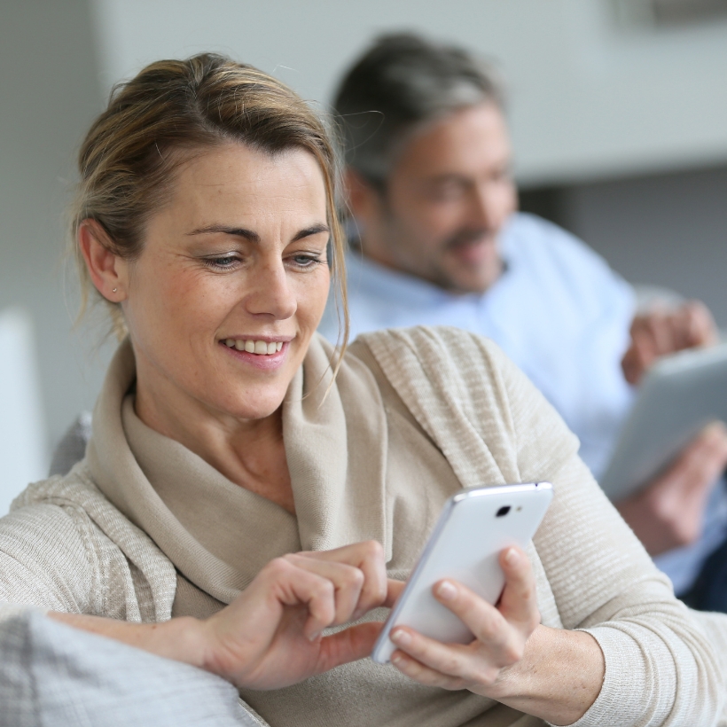 Woman looking at her phone with man in the back also looking at phone