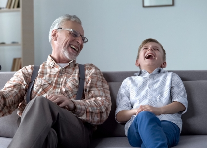 Older man and grandson sat on sofa laughing