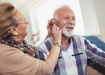 Elderly man having his hearing aids put in by elderly woman