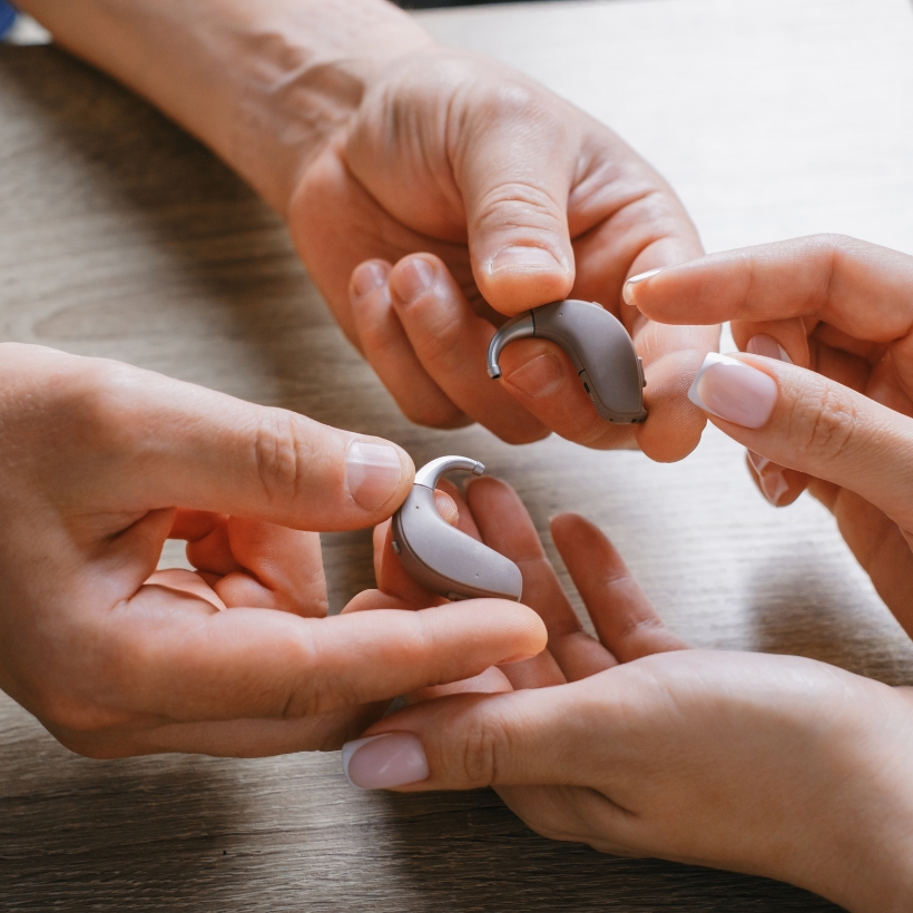 Two sets of hands both holding hearing aids