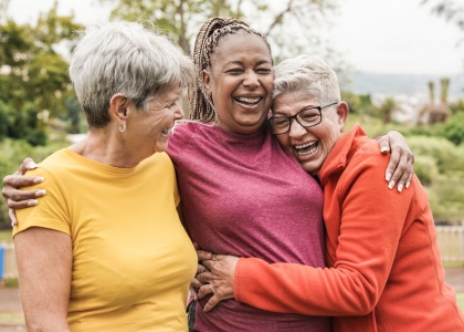 Three older women smiling and hugging each other