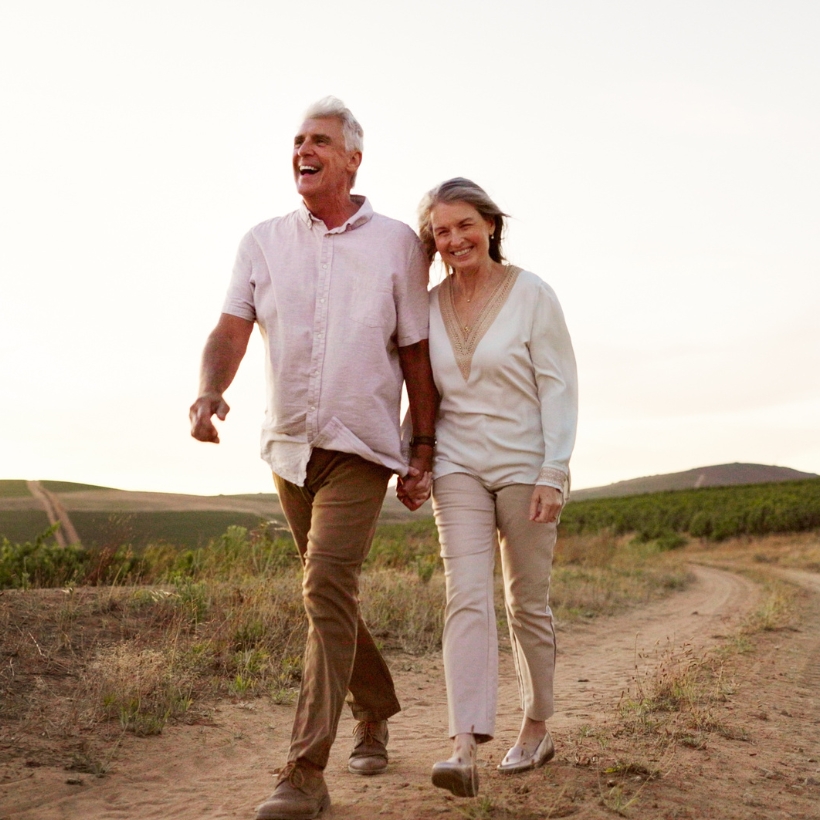 Older man and woman holding hands walking on a dirt path
