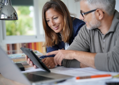 Middle aged woman with man looking at tablet while sat on table