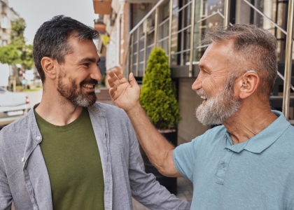 Middle aged man wearing hearing aids meeting his friend and smiling in the street