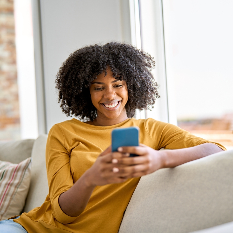 Lady in a mustard yellow jumper sat on sofa looking at phone