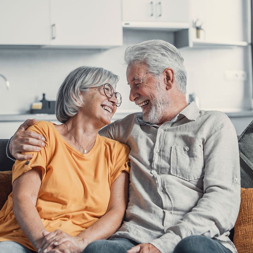 Older couple sat together smiling on sofa