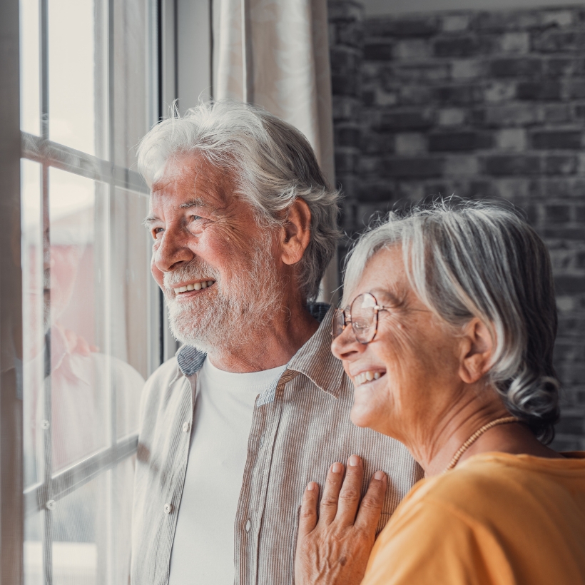 Older couple stood together looking outside the window