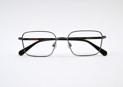 Rectangular metal eyeglasses with black temples resting on a white surface, GANT branding visible on the frame.