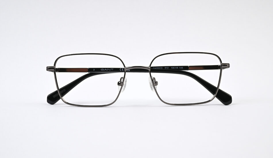 Rectangular metal eyeglasses with black temples resting on a white surface, GANT branding visible on the frame.