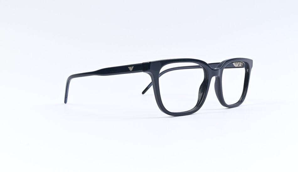 Black rectangular eyeglasses resting on a white surface, viewed from the side.